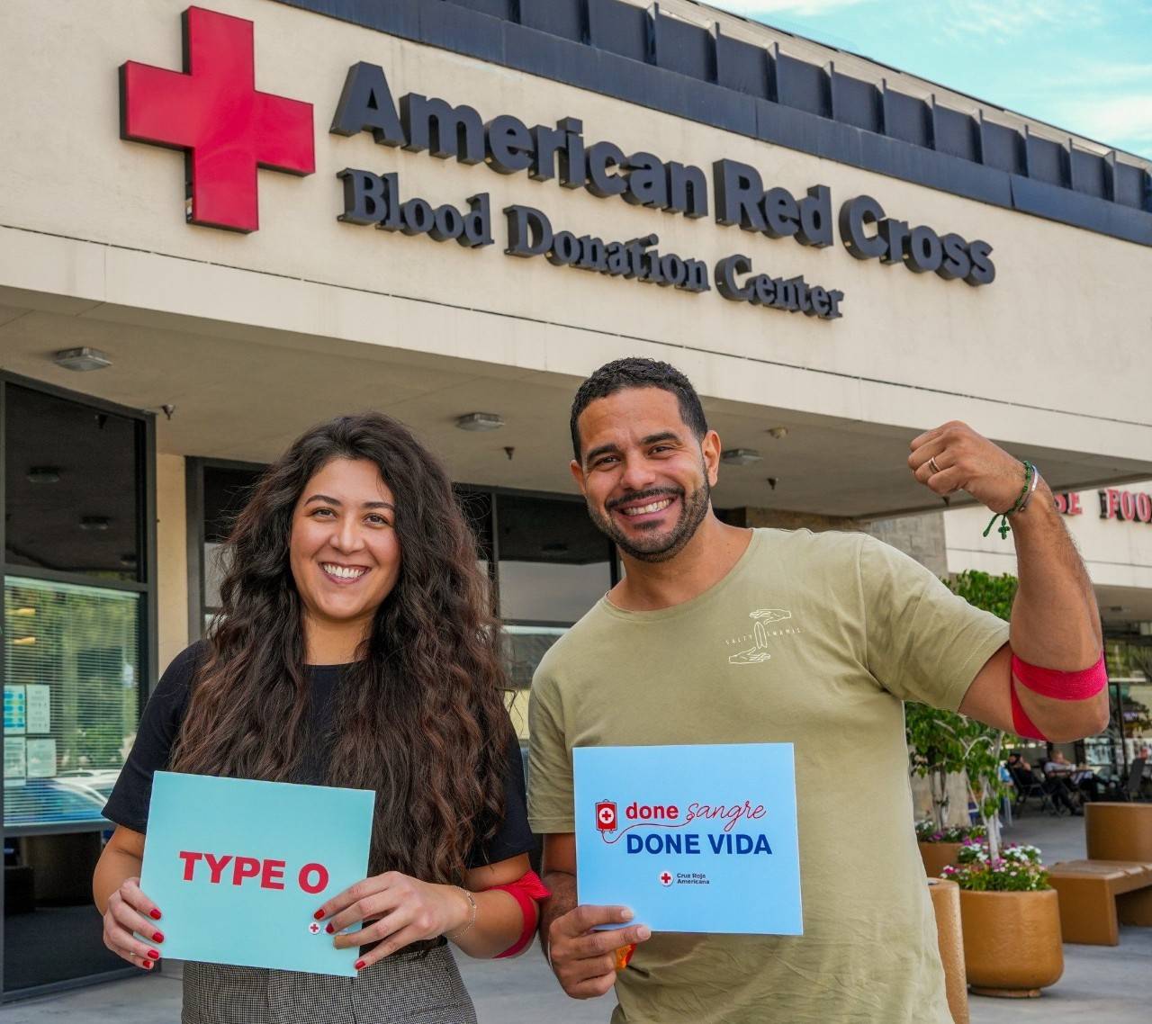 Hombre y mujer sonriendo mientras sostienen letreros que dicen que donaron sangre en la Cruz Roja Americana.